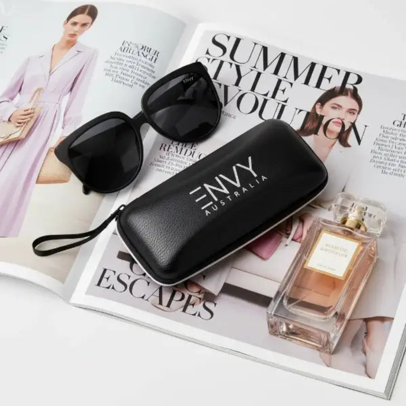 Annabelle oversized Black sunglasses with case and perfume bottle on a magazine