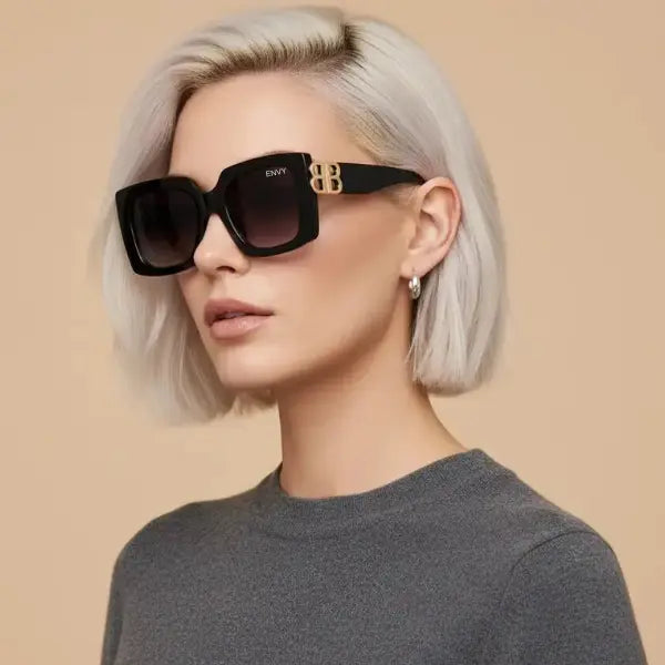 Woman wearing black sunglasses with gold accents on a beige background