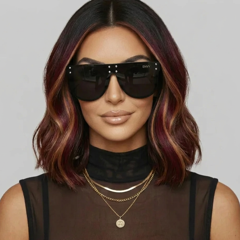 A woman wears oversized square top sunglasses called Celebrity Oversized with a thick black frame and dark lenses. The brand name 'ENVY' is visible on the top corner of the frame.