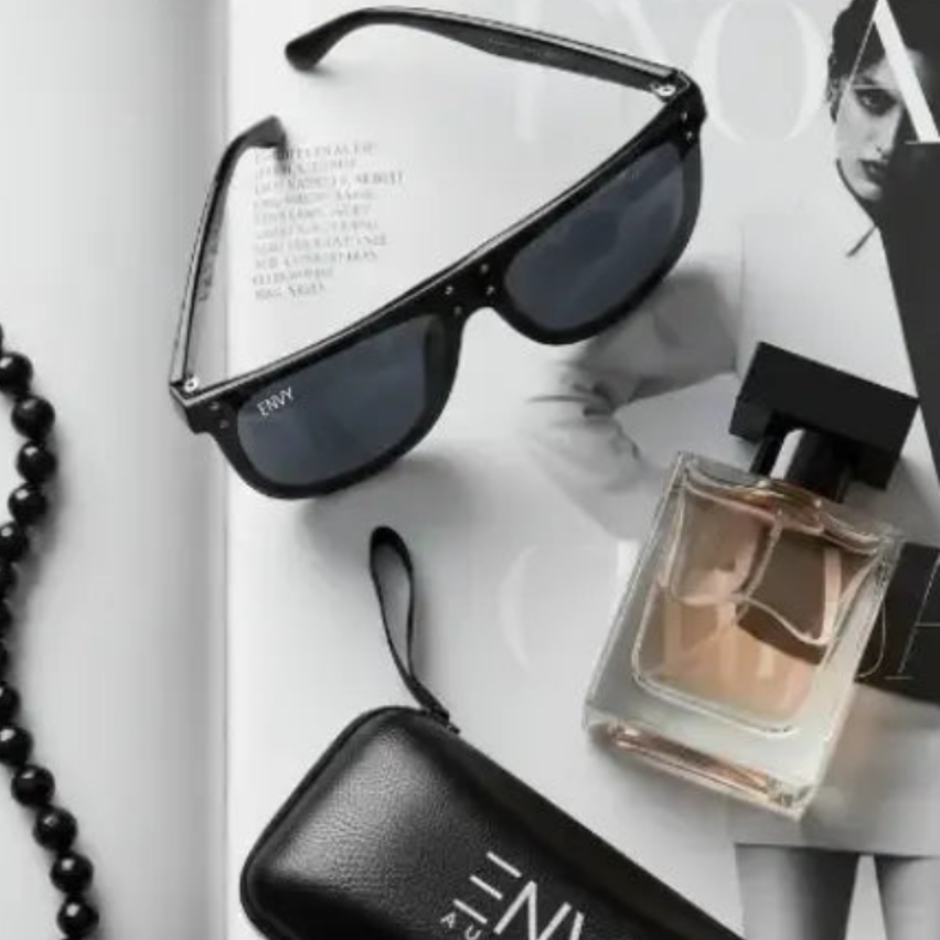 Flat lay photo of oversized square top sunglasses called Celebrity Oversized with a thick black frame and dark lenses. The brand name 'ENVY' is visible on the top corner of the frame.