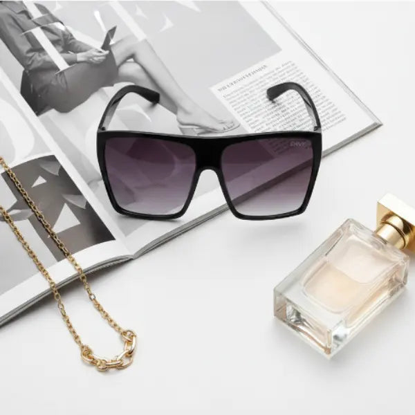 Black Envy sunglasses, gold necklace, and perfume bottle on a magazine