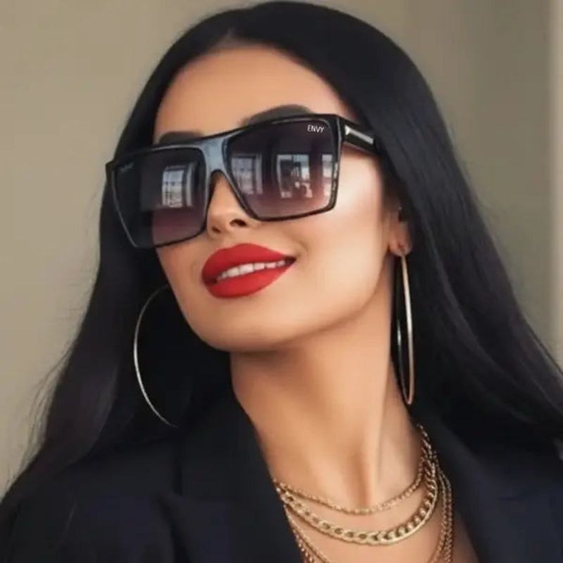 Woman wearing Envy Luxe black sunglasses and gold jewelry with a neutral background