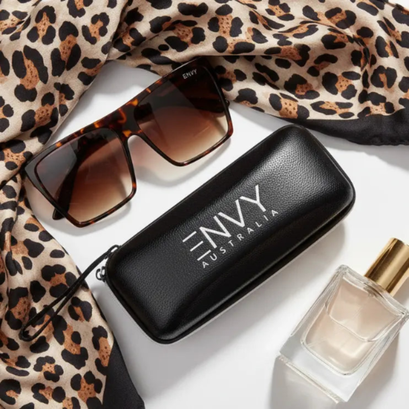 Envy Luxe Leopard Sunglasses and perfume bottle with Envy Australia case on a leopard print fabric background