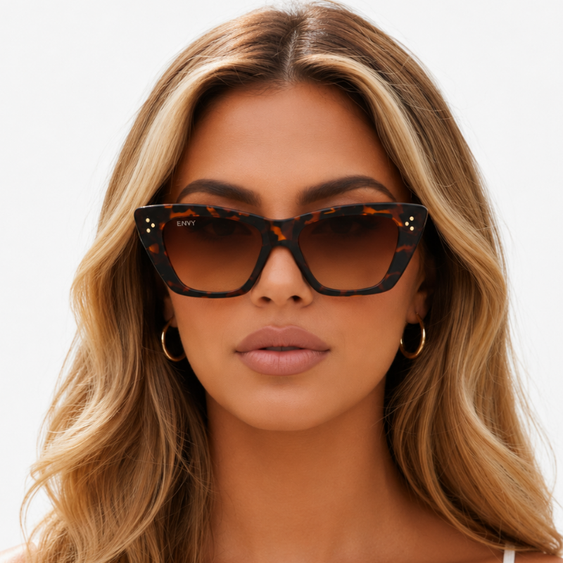 A close-up of a woman wearing Envy brand cat-eye sunglasses with a dark tortoiseshell pattern and brown lenses, set against a clean white background.