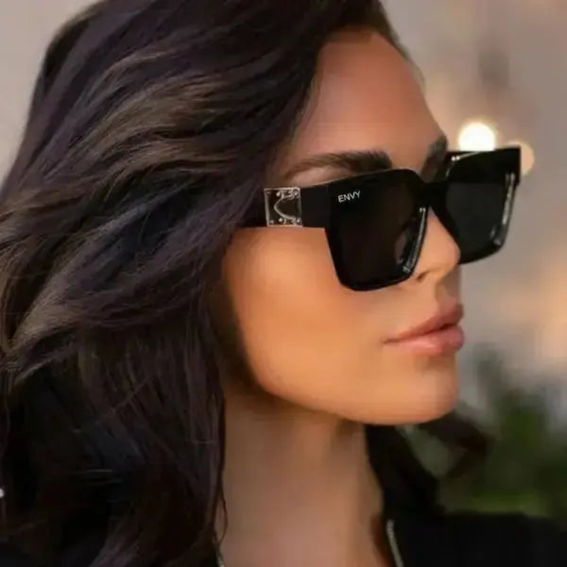 Person wearing London Look black sunglasses with 'ENVY' branding, blurred background