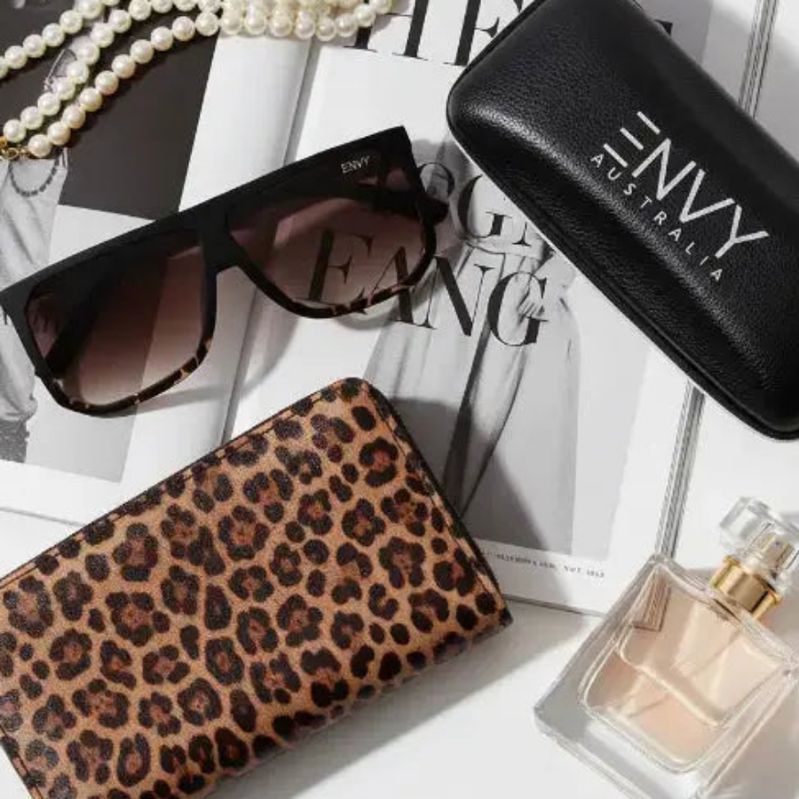 Leopard print wallet, Luxe Escape Leopard sunglasses, perfume bottle, and 'ENVY Australia' case on a magazine