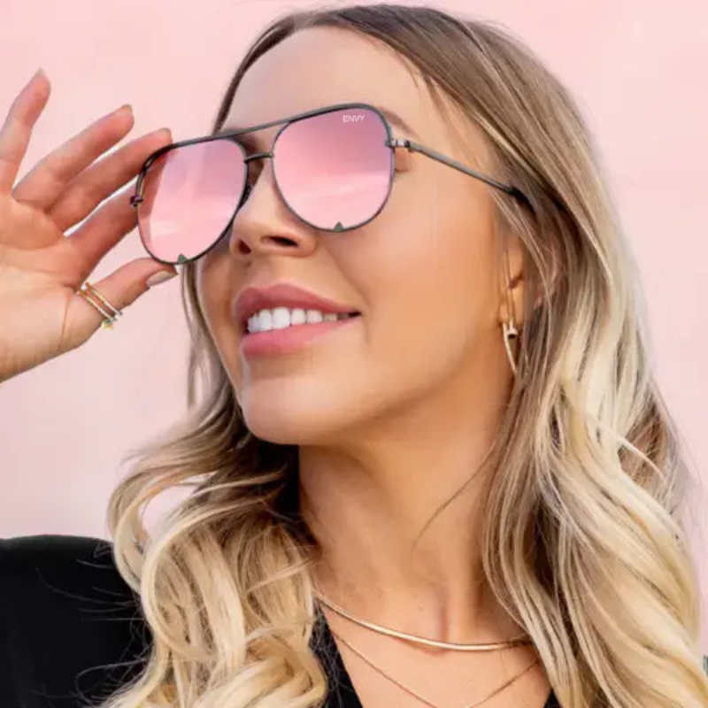 Woman wearing Mirror Shine pink-tinted Envy sunglasses with a blurred background
