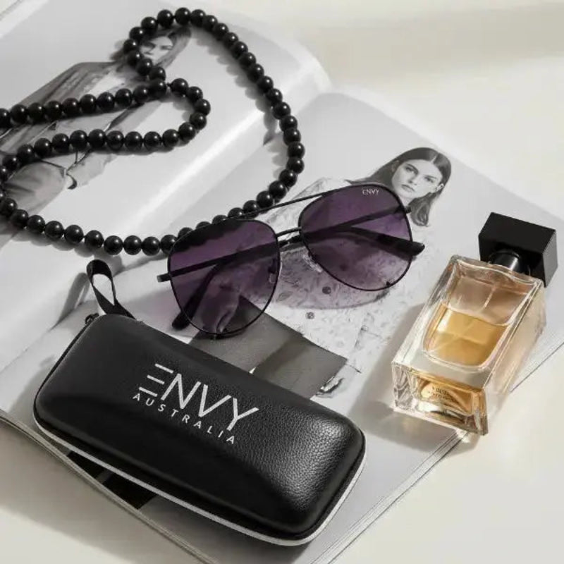 Envy Ombre Pilot Black Black 'ENVY Australia' case, sunglasses, and perfume bottle on a magazine