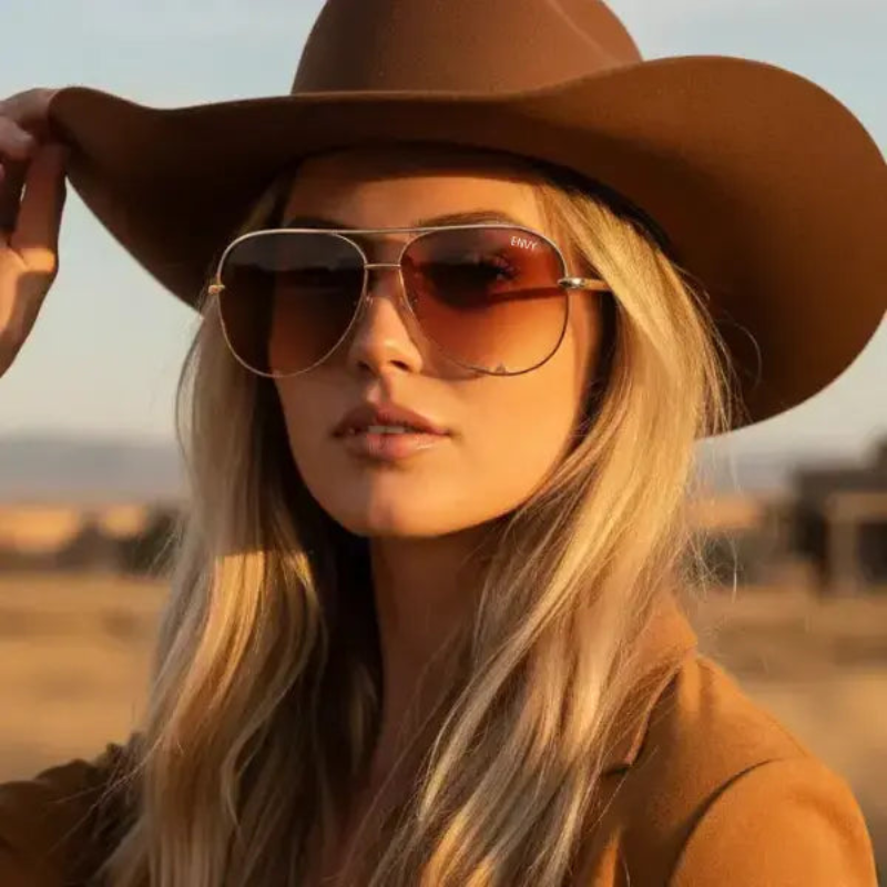 Woman wearing a brown hat and OmbrePIlot Tan sunglasses with a blurred natural background