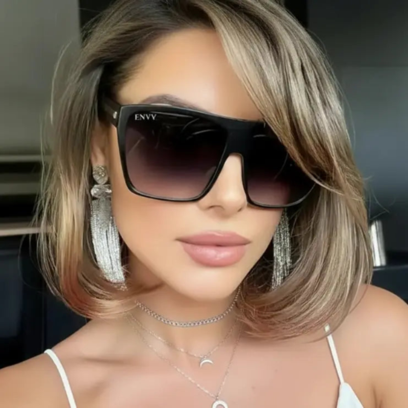 Woman wearing Sachi black sunglasses with 'ENVY' branding, indoors.
