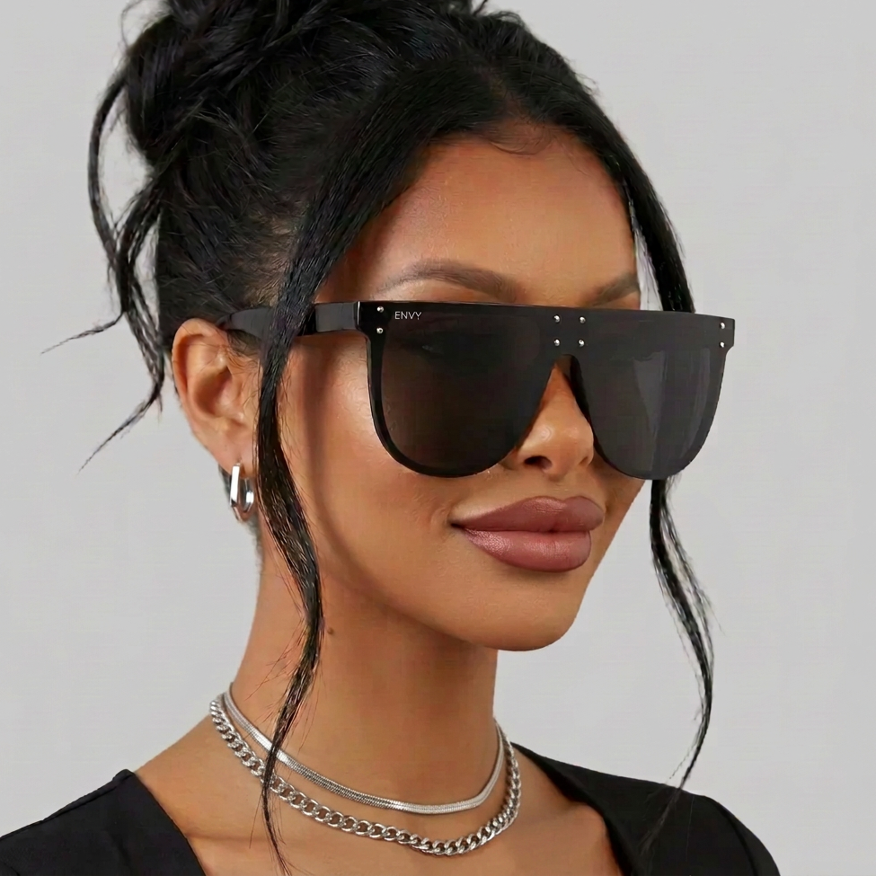 A woman with her hair in a bun wears oversized square top sunglasses called Celebrity Oversized with a thick black frame and dark lenses. The brand name 'ENVY' is visible on the top corner of the frame.