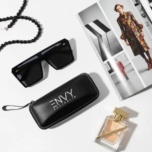 Black sunglasses with 'ENVY Australia' case, necklace, and perfume bottle on a white background