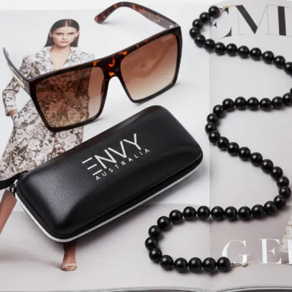 Envy Sunglasses with black case and black beaded necklace on a magazine